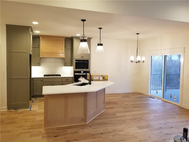 kitchen featuring sink, stainless steel appliances, light hardwood / wood-style flooring, decorative light fixtures, and a kitchen island with sink