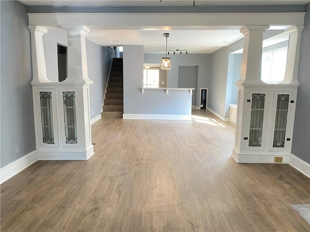 unfurnished living room with decorative columns, hardwood / wood-style flooring, and a healthy amount of sunlight