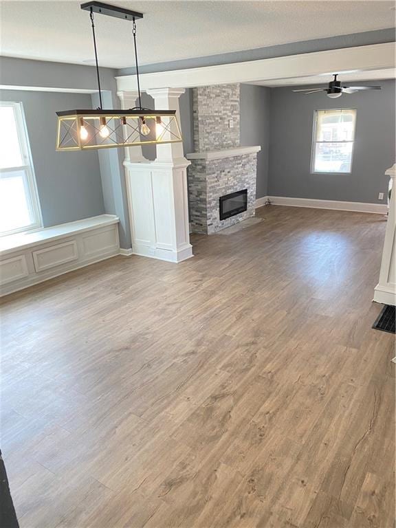 unfurnished living room featuring a stone fireplace, ceiling fan, and light hardwood / wood-style flooring