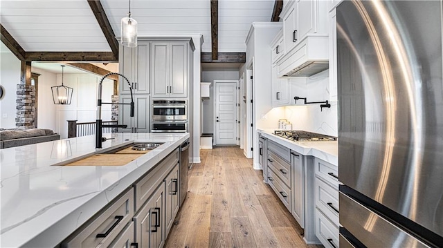 kitchen with pendant lighting, stainless steel appliances, beamed ceiling, and light hardwood / wood-style flooring