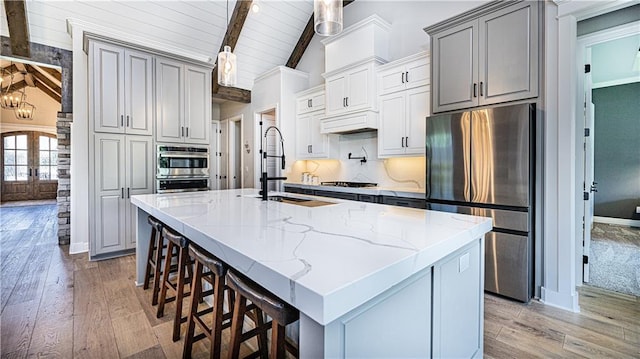 kitchen featuring an island with sink, sink, appliances with stainless steel finishes, and vaulted ceiling with beams