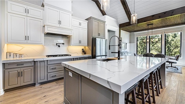 kitchen with a kitchen island with sink, wood ceiling, hanging light fixtures, custom exhaust hood, and light wood-type flooring