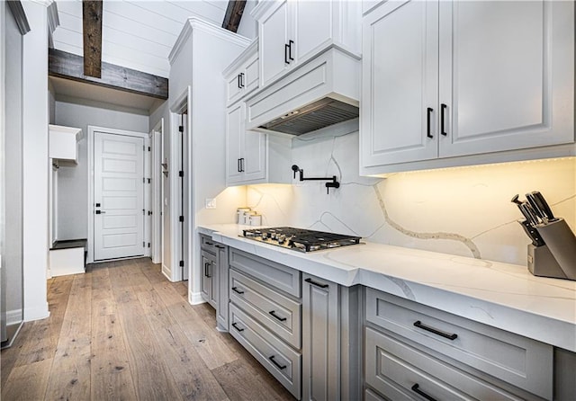 kitchen featuring stainless steel gas stovetop, premium range hood, light stone countertops, beam ceiling, and light hardwood / wood-style floors