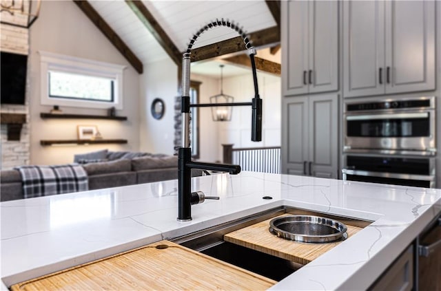 kitchen featuring double oven, gray cabinetry, and vaulted ceiling with beams