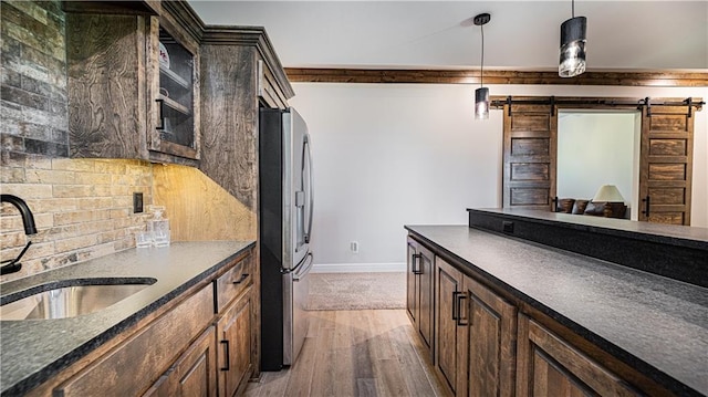 kitchen with light hardwood / wood-style flooring, backsplash, sink, stainless steel fridge with ice dispenser, and a barn door