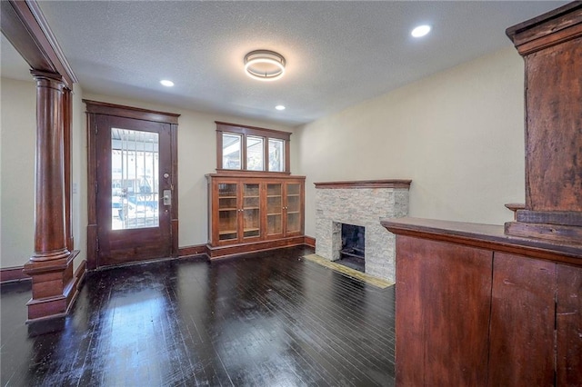 foyer entrance with a fireplace, dark wood-type flooring, a textured ceiling, and decorative columns