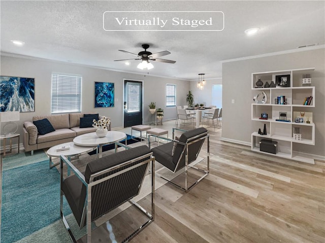 living room featuring ornamental molding, a textured ceiling, ceiling fan, and light hardwood / wood-style floors