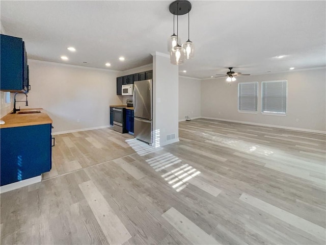 kitchen with ceiling fan with notable chandelier, butcher block countertops, ornamental molding, and stainless steel appliances