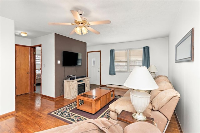 living area featuring a textured ceiling, baseboards, ceiling fan, wood finished floors, and a baseboard heating unit