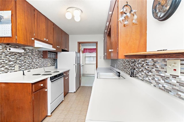 kitchen featuring light countertops, a sink, brown cabinets, under cabinet range hood, and white appliances