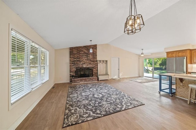 living room featuring wood-type flooring, vaulted ceiling, ceiling fan with notable chandelier, and a brick fireplace