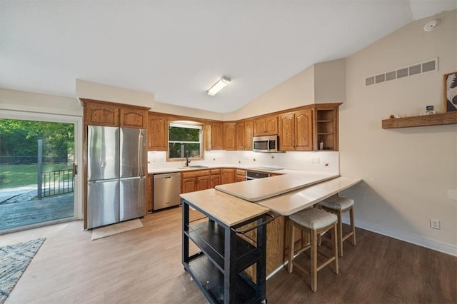 kitchen featuring light wood-type flooring, kitchen peninsula, a breakfast bar, appliances with stainless steel finishes, and lofted ceiling