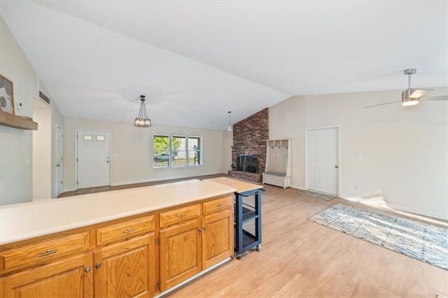 kitchen with light wood-type flooring, pendant lighting, ceiling fan with notable chandelier, a brick fireplace, and lofted ceiling