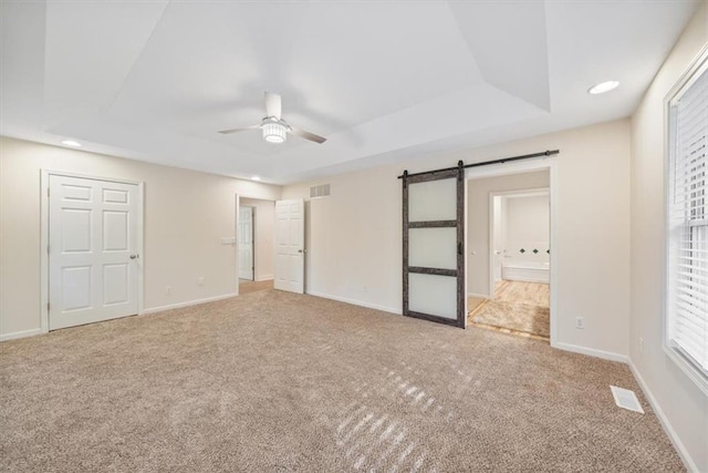 unfurnished bedroom with a barn door, ceiling fan, ensuite bath, and carpet