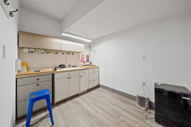 kitchen featuring white cabinets, wood counters, light wood-type flooring, tasteful backsplash, and a textured ceiling