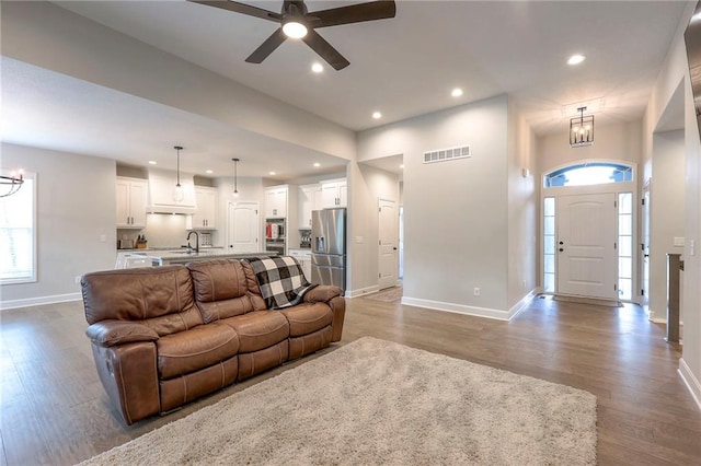 living room with wood-type flooring, ceiling fan with notable chandelier, and sink