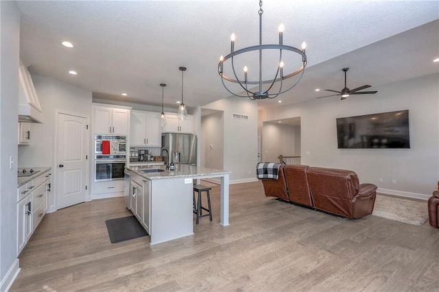 kitchen featuring an island with sink, white cabinets, hanging light fixtures, stainless steel appliances, and ceiling fan