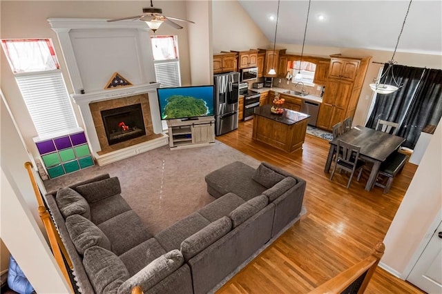 living room with ceiling fan, sink, high vaulted ceiling, light hardwood / wood-style floors, and a fireplace