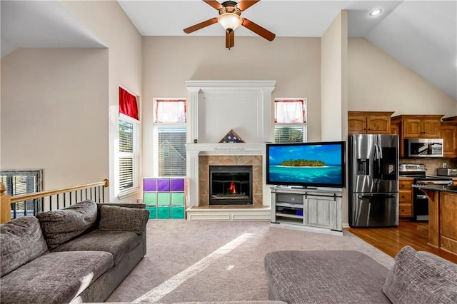 living room featuring high vaulted ceiling, ceiling fan, light carpet, and a tile fireplace