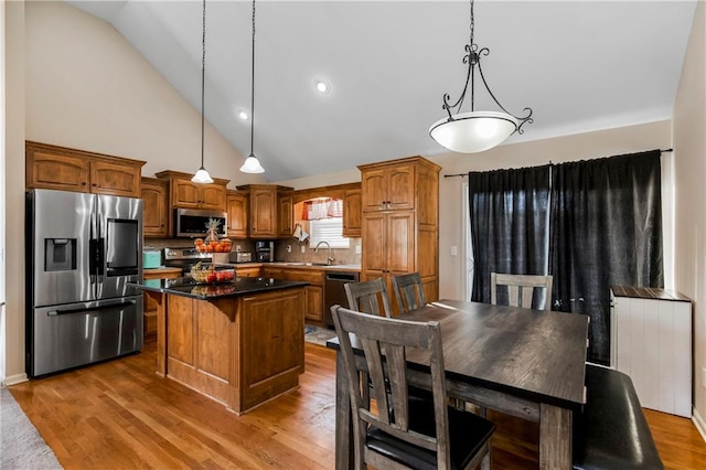 kitchen with hardwood / wood-style floors, a center island, backsplash, decorative light fixtures, and stainless steel appliances