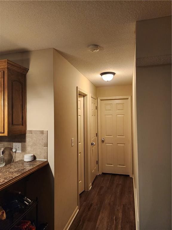 corridor with a textured ceiling and dark wood-type flooring