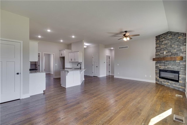 unfurnished living room featuring ceiling fan, a stone fireplace, dark hardwood / wood-style flooring, and vaulted ceiling