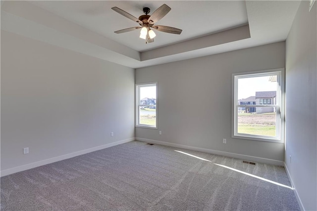 spare room with a tray ceiling, light carpet, and ceiling fan