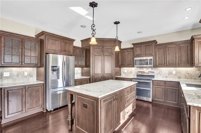 kitchen with appliances with stainless steel finishes, dark hardwood / wood-style flooring, a kitchen island, and hanging light fixtures