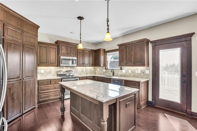 kitchen featuring appliances with stainless steel finishes, a kitchen island, decorative light fixtures, dark wood-type flooring, and light stone counters