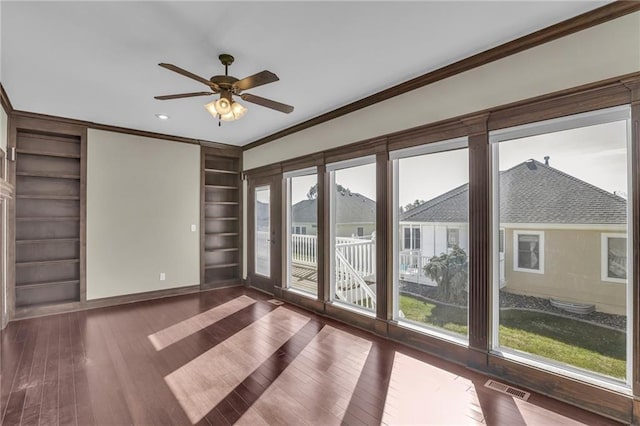 empty room featuring dark wood-type flooring, ceiling fan, built in features, and ornamental molding