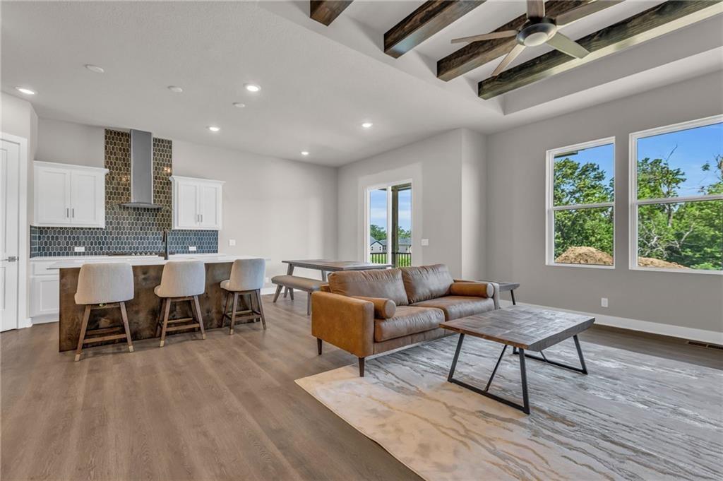 living room featuring wood-type flooring, sink, beam ceiling, and ceiling fan