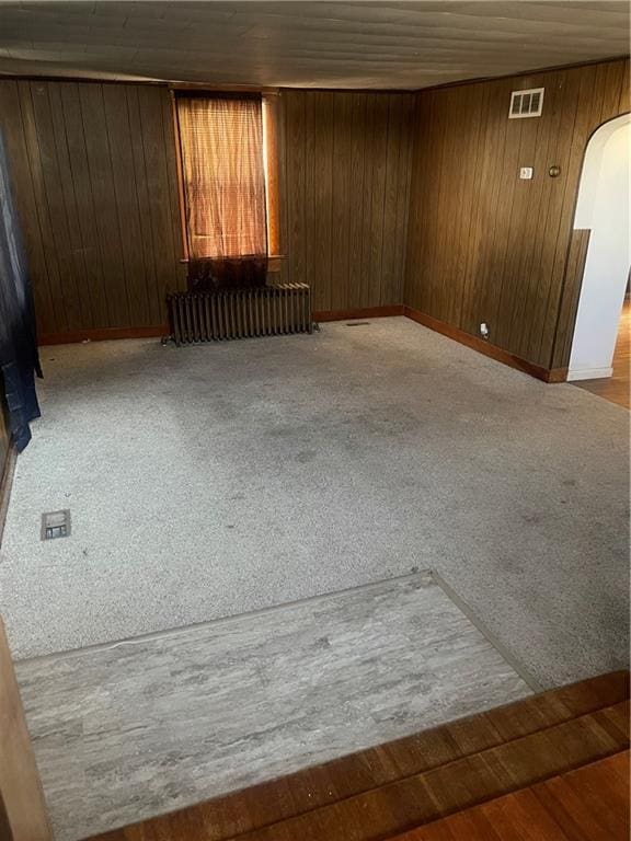 carpeted empty room featuring wood walls and radiator heating unit