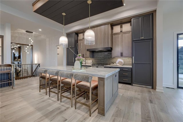 4511 W 136th St, Leawood, KS 66224 - kitchen featuring a kitchen breakfast bar, a raised ceiling, light wood-type flooring, a center island with sink, and backsplash