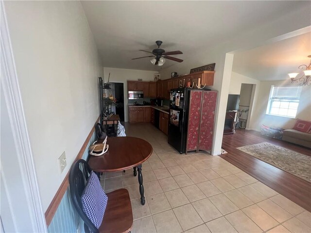 interior space featuring light hardwood / wood-style flooring, ceiling fan with notable chandelier, and black fridge