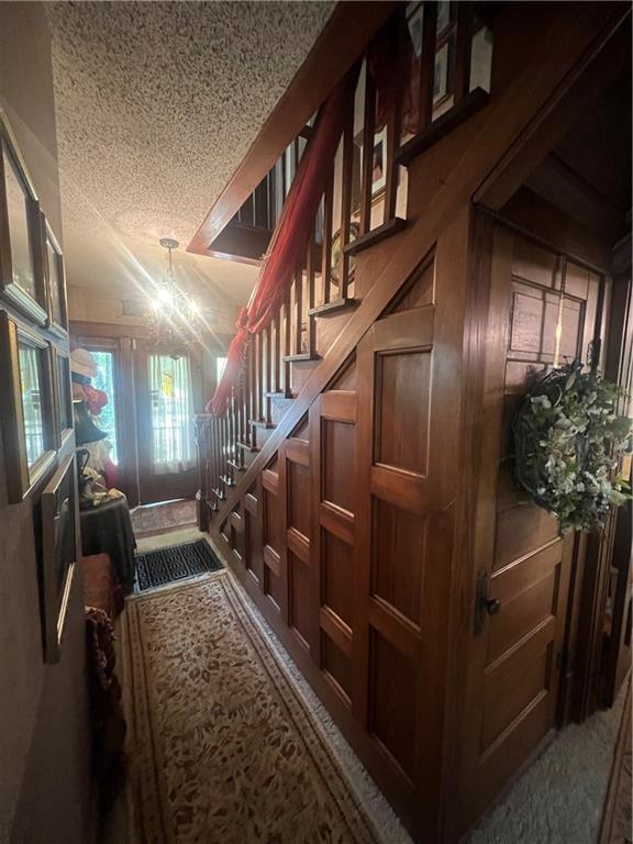 stairway featuring a textured ceiling, carpet flooring, wood walls, and a chandelier