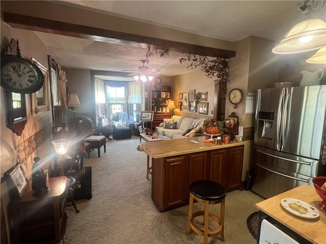 kitchen with a textured ceiling, a kitchen breakfast bar, stainless steel fridge, light colored carpet, and ceiling fan