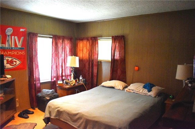 bedroom with multiple windows, a textured ceiling, and wooden walls