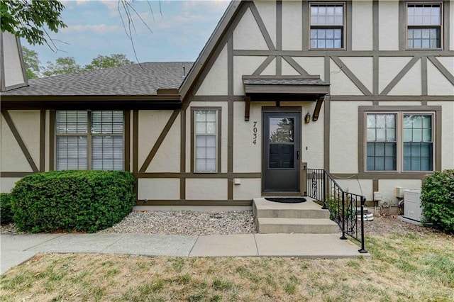 doorway to property featuring a yard, a shingled roof, and stucco siding