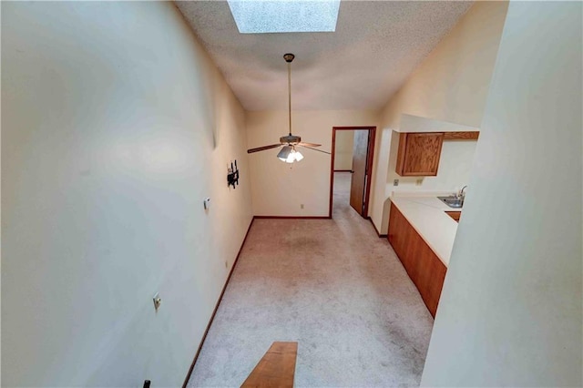 interior space featuring a skylight, brown cabinetry, light colored carpet, light countertops, and a textured ceiling