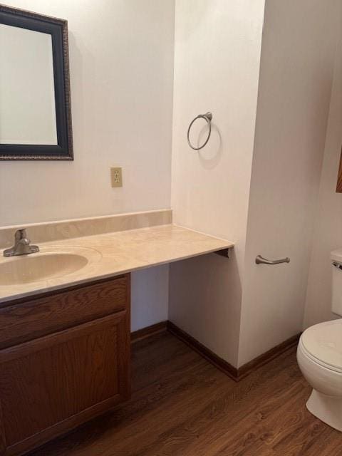 half bathroom featuring wood finished floors, vanity, toilet, and baseboards