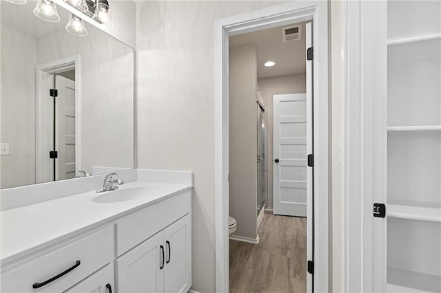 bathroom featuring hardwood / wood-style floors, vanity, a shower with shower door, and toilet