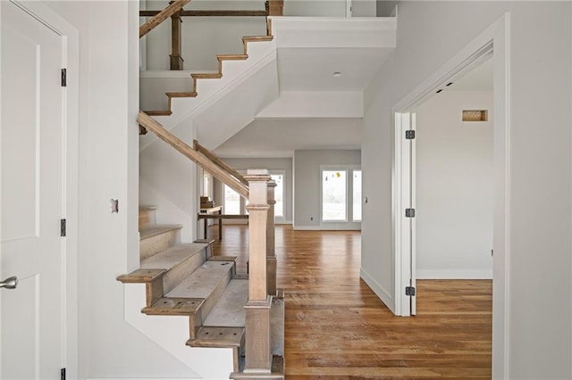 entrance foyer featuring stairway, a towering ceiling, baseboards, and wood finished floors