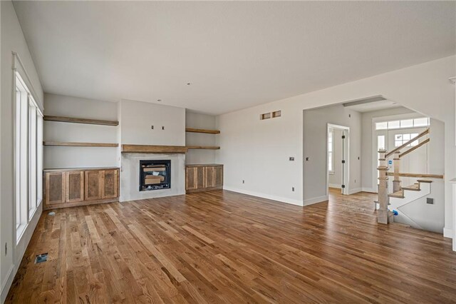 unfurnished living room with stairs, visible vents, wood finished floors, and a fireplace