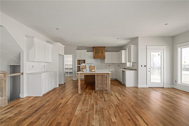 kitchen featuring a kitchen island, open floor plan, a breakfast bar area, wood finished floors, and white cabinets