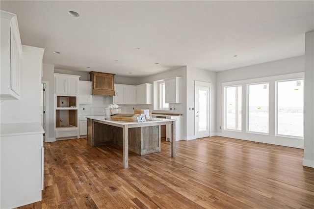 kitchen featuring a center island, baseboards, a kitchen bar, wood finished floors, and white cabinetry