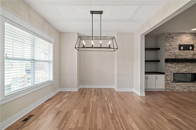 unfurnished dining area with visible vents, built in shelves, light wood-style floors, and a stone fireplace