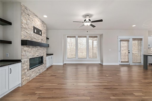 unfurnished living room featuring baseboards, light wood-style floors, a stone fireplace, and ceiling fan