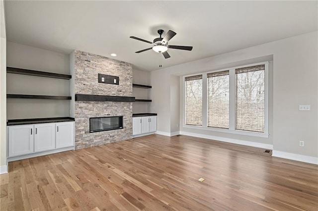 unfurnished living room featuring a stone fireplace, light wood-style flooring, baseboards, and ceiling fan