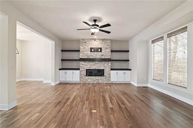 unfurnished living room with light wood-style flooring, a fireplace, baseboards, and ceiling fan