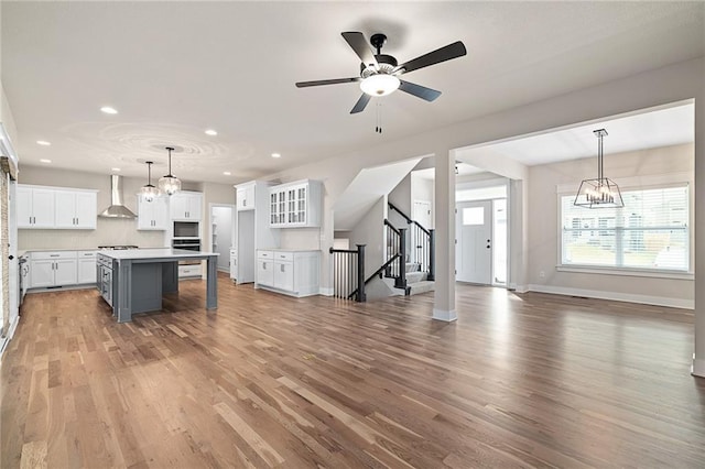 kitchen with light wood-style flooring, a kitchen island, open floor plan, white cabinets, and wall chimney range hood